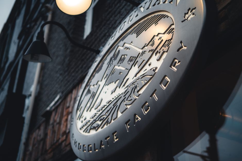 A modern, illuminated sign for a chocolate factory photographed at dusk, showcasing urban architecture.